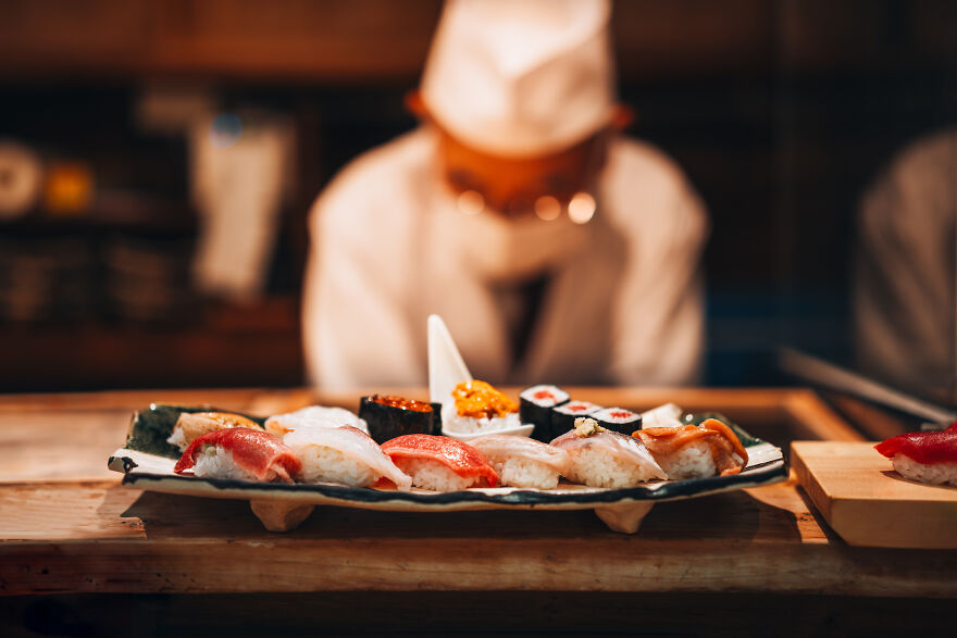 A chef in a white uniform preparing a plate of fresh, vibrant sushi, featuring various types of Japanese things like nigiri and rolls.