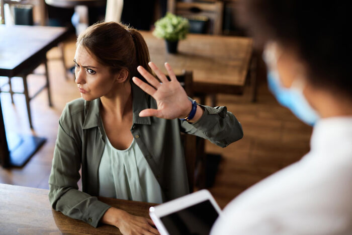 Woman makes a stop gesture to a person wearing a mask; a scene of chaos or a hilarious engagement story.