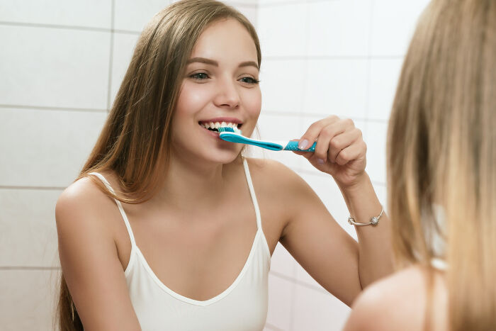 Young woman smiling while brushing teeth in bathroom mirror