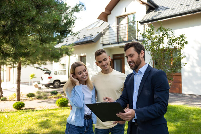 Couple discussing home purchase with agent outside house on January 6