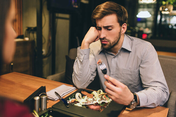 A man looks bored at a dinner table, resting his head on his hand and holding a fork. Engagement Stories.