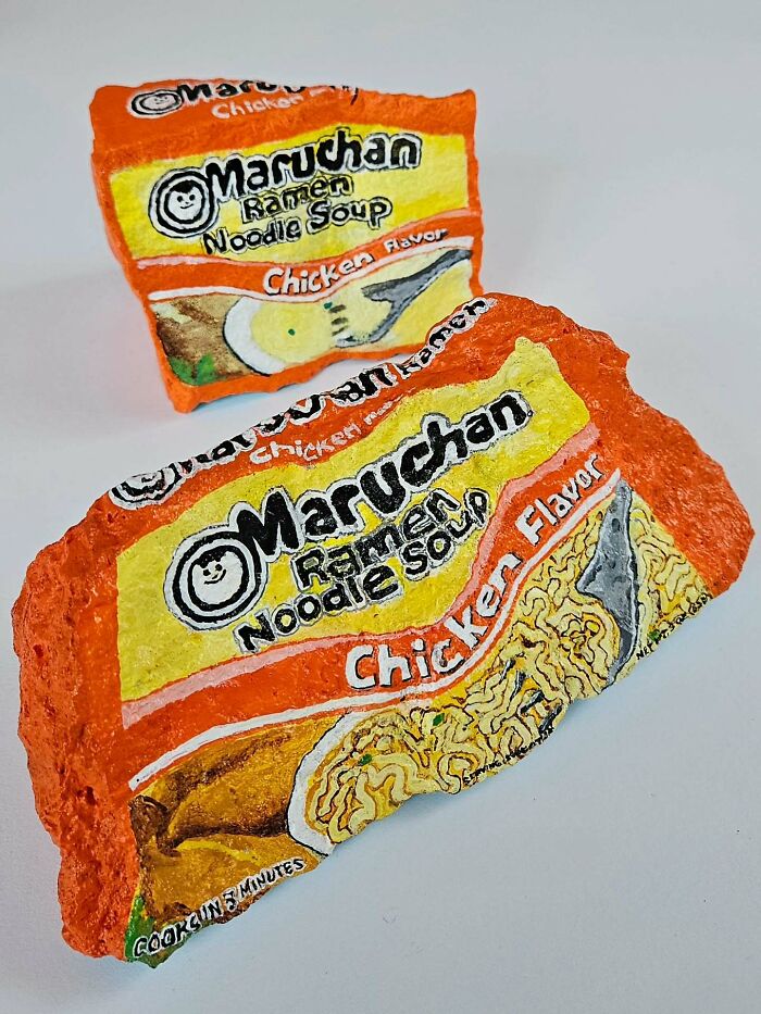 Two rocks painted to look like Maruchan Chicken Ramen noodle soup packages. Iconic foods turned into stone creations.