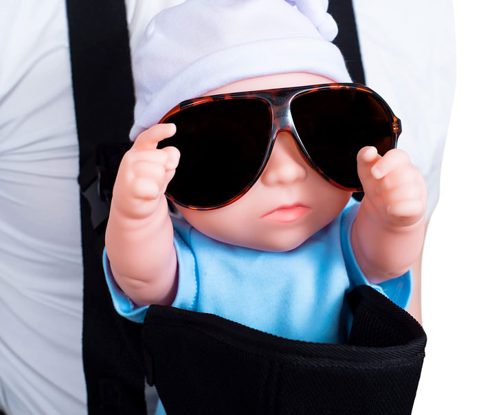 A baby doll in a carrier wears a white hat and large sunglasses, looking cool. Perhaps one of the weirdest packages.