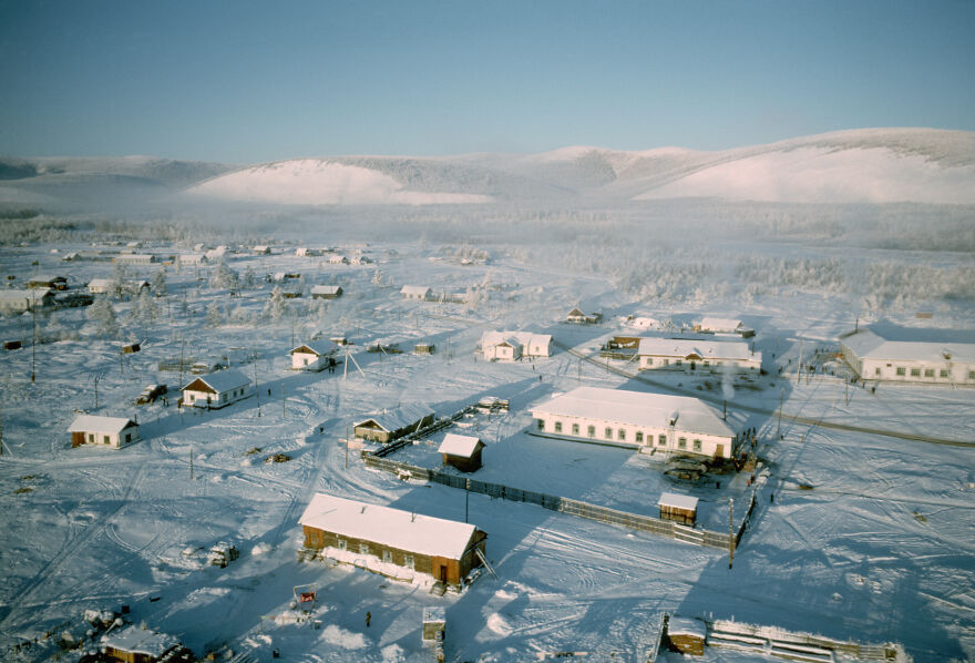 An aerial view of a snow-covered village, nestled among hills and forests. Isolated places like this leave civilization behind.