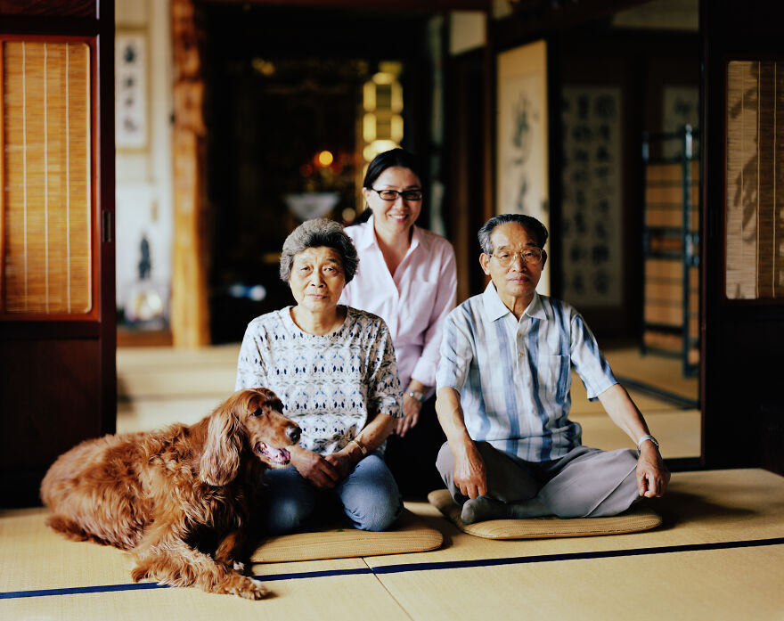 A Japanese family, two elders and a younger woman, sitting with a dog on traditional mats indoors, showcasing Japanese things.