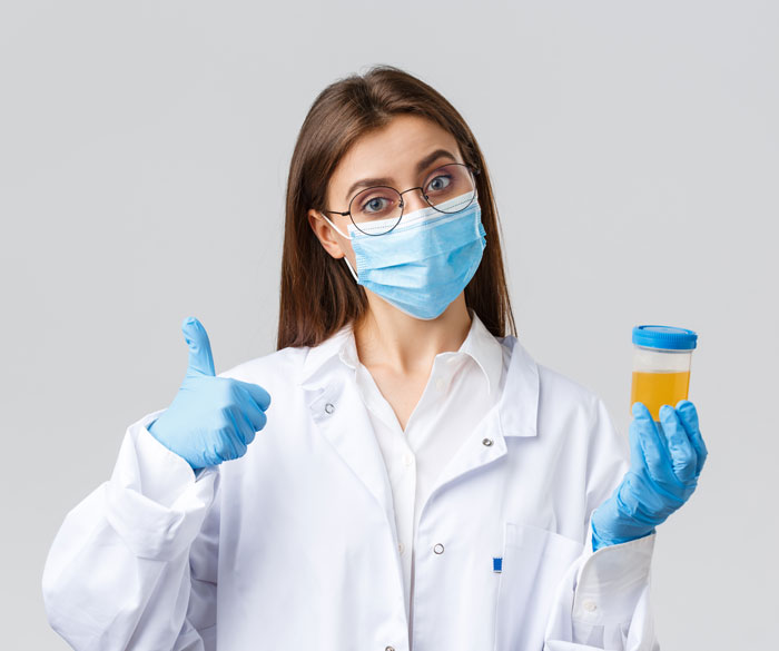 A female doctor in a mask, gloves, and lab coat holds a urine sample and gives a thumbs-up. Wrong facts on Reddit.