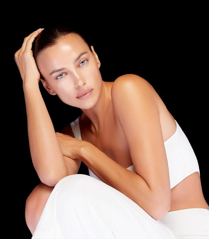 Irina Shayk with a male body, wearing white, posing against a black background, looking directly at the camera. Irina Shayk with a male body, wearing white, posing against a black background, looking directly at the camera.