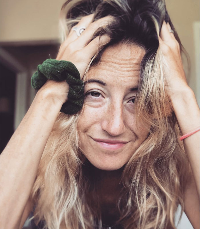A woman with blonde hair, a green scrunchie on her wrist, and a light smile, running her hands through her hair after a relationship ends due to a ChatGPT scandal.
