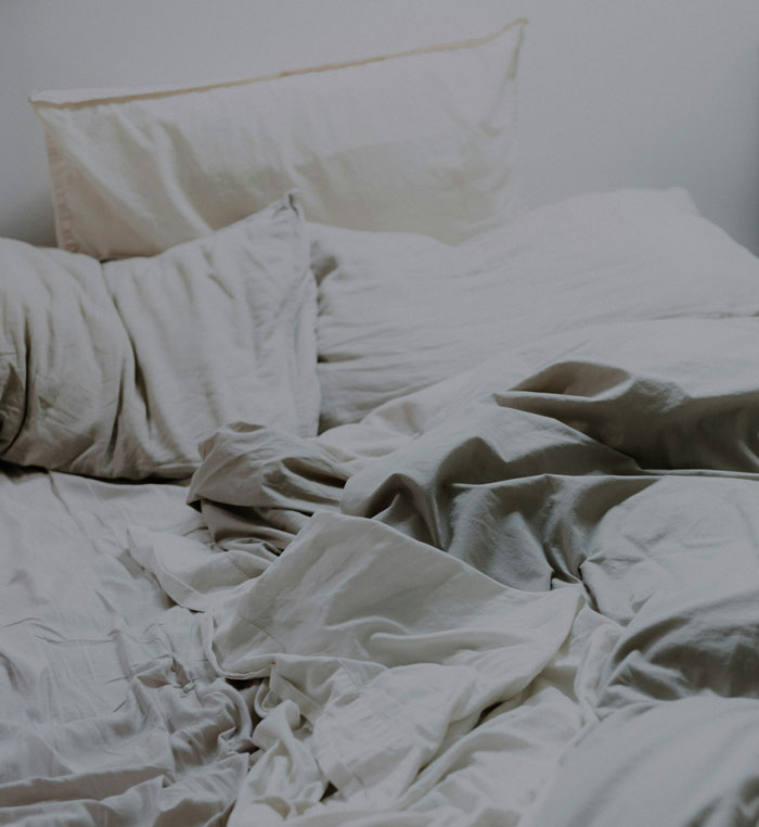 An unmade bed with crumpled, light-colored sheets and pillows. A simple comfort often seen as luxury by those who grew up poor.