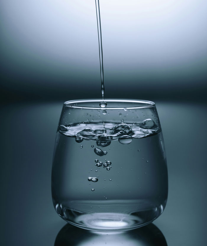 Water droplets falling into glass of water representing glitch in the matrix liquid