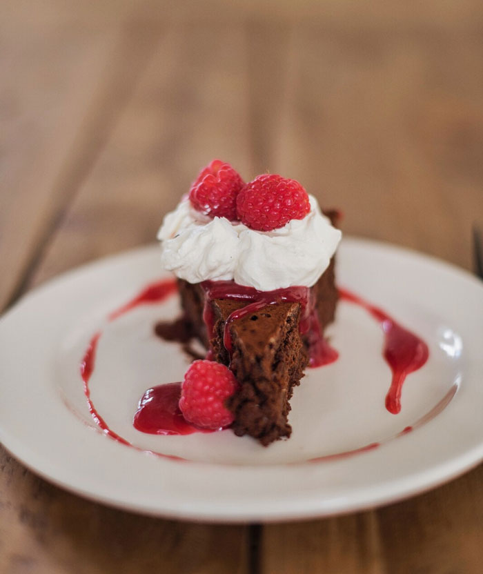 Artisinal chocolate dessert topped with whipped cream and raspberries