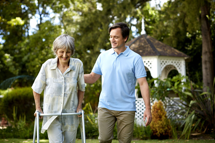 Man assisting elderly woman walking outdoors for emotional boost