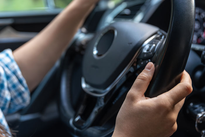 Person gripping car steering wheel while driving with focus on hand