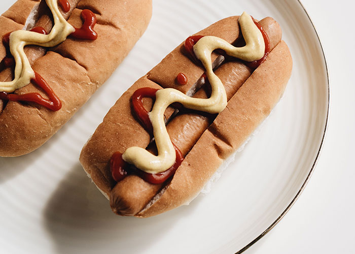 Two hot dogs with mustard and ketchup on a white plate