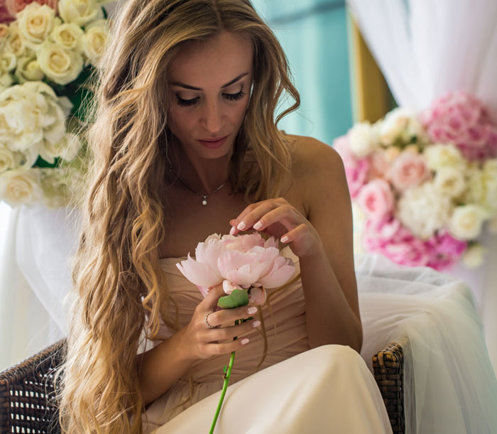 Bride in wedding dress examining soft pink flower before ceremony