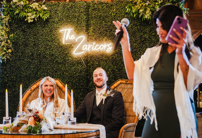 Wedding photographers capture bride and groom sitting under neon sign at reception
