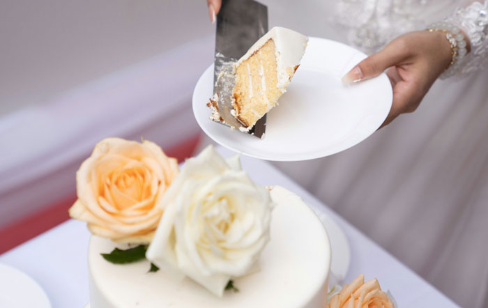Bride serving a slice of wedding cake decorated with fresh roses Bride serving a slice of wedding cake decorated with fresh roses