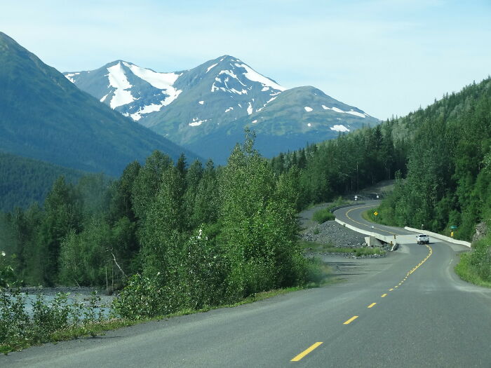 Winding mountain road with snow-capped peaks and dense forest