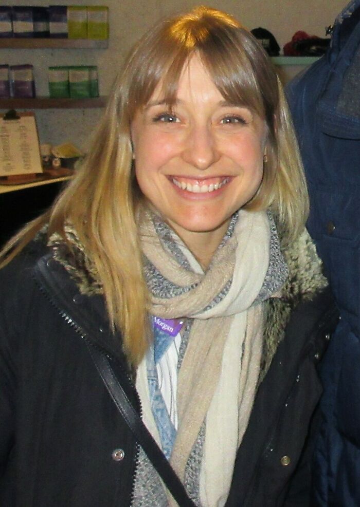 Smiling woman wearing a scarf and jacket in an indoor setting