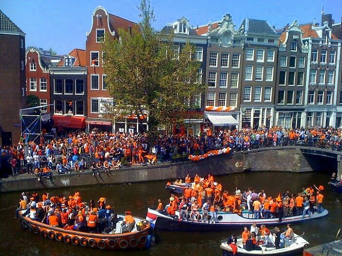 Crowds wearing orange celebrating on boats in city canal festival