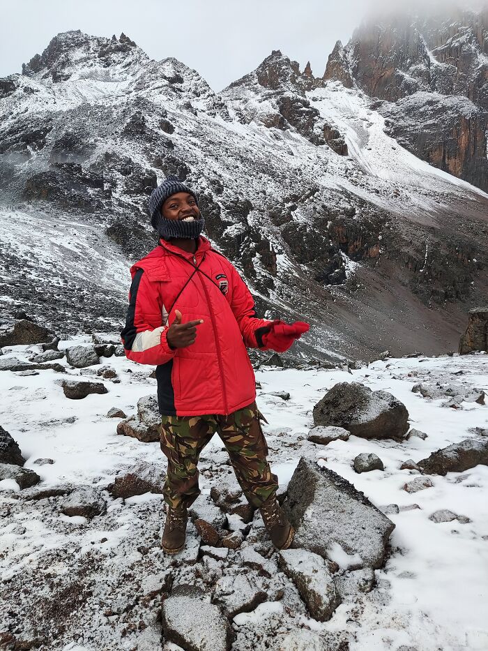 Smiling person in red jacket on snowy rocky path with stunning mountain views