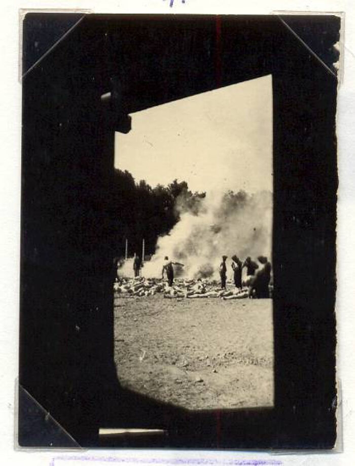 Vintage black and white photo showing people near a smoke pile seen through a dark doorway