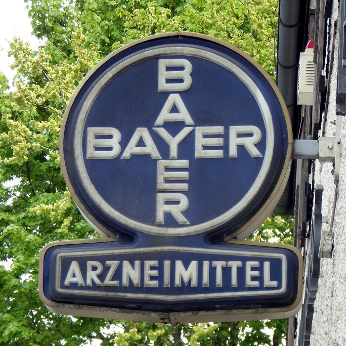 Bayer logo on vintage Arzneimittel sign with green tree background