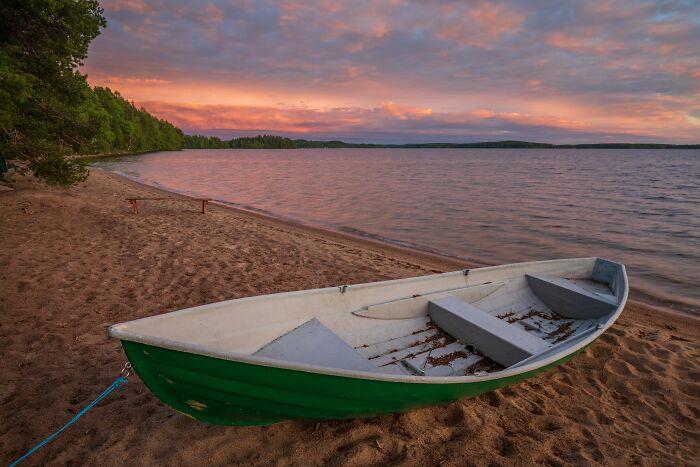 Small green boat on lake shore at sunset with stunning water views
