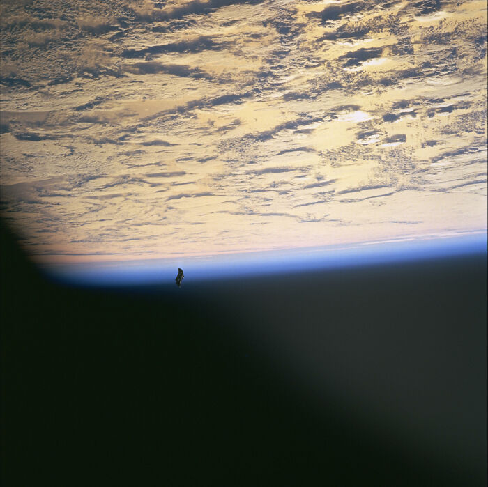 Satellite floating above Earth with visible cloud cover and horizon