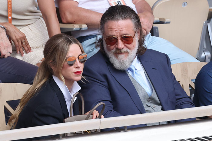 Russell Crowe wearing suit and sunglasses seated next to woman at event