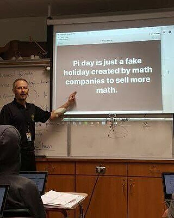 A teacher points to a funny math meme on a projector screen, saying Pi Day is a fake holiday to sell more math.
