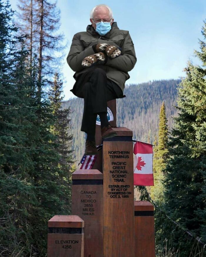 Bernie Sanders sitting on hiking trail marker at Northern Terminus of Pacific Crest Trail