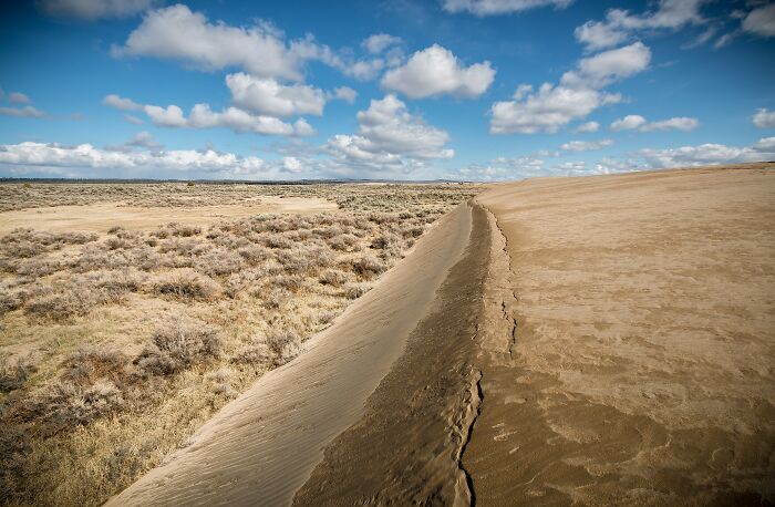 Wide arid desert landscape meeting sand dunes under cloudy sky