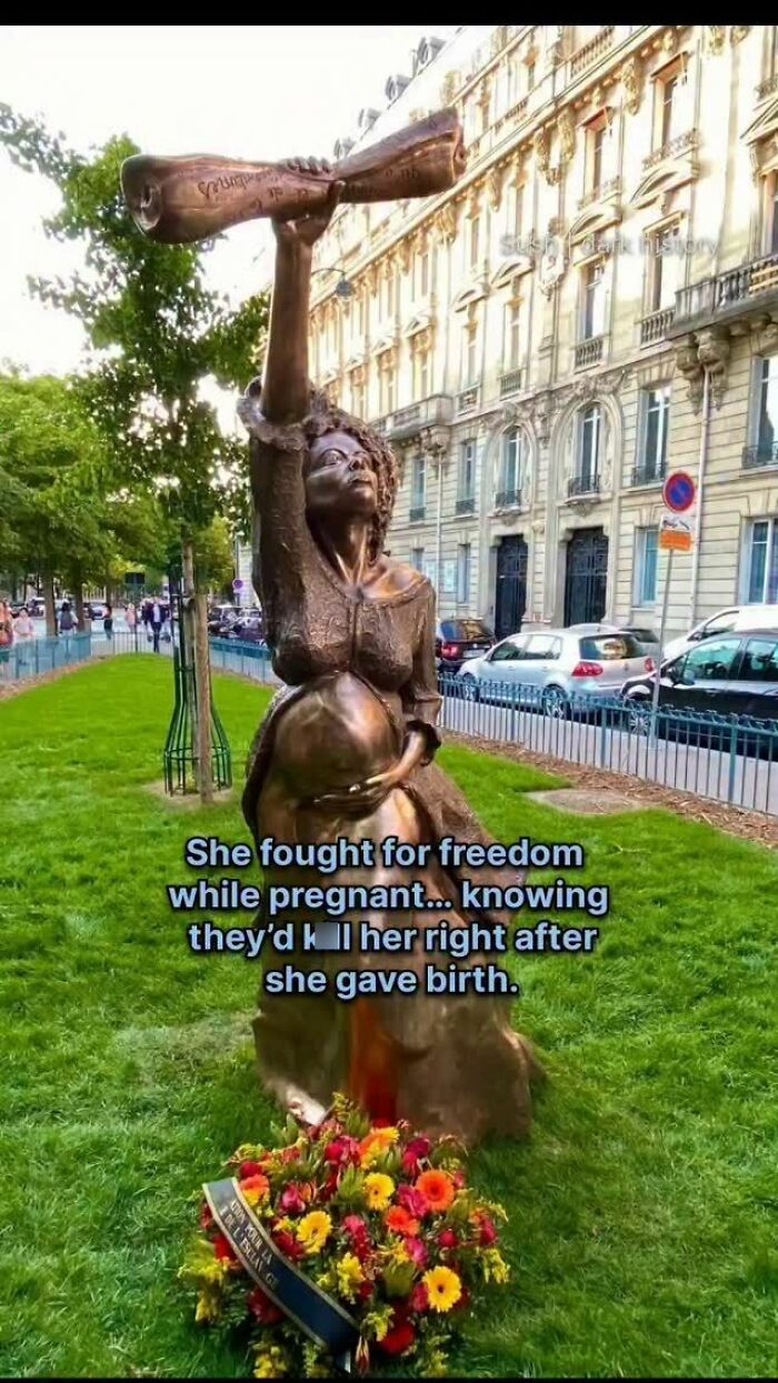 Statue of pregnant woman fighting for freedom in historical context with flowers at base