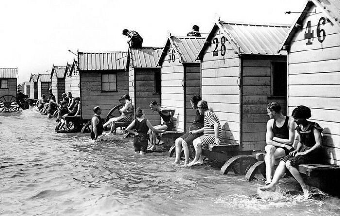 Vintage beach bathhouses with people in old-fashioned swimwear sitting by the sea