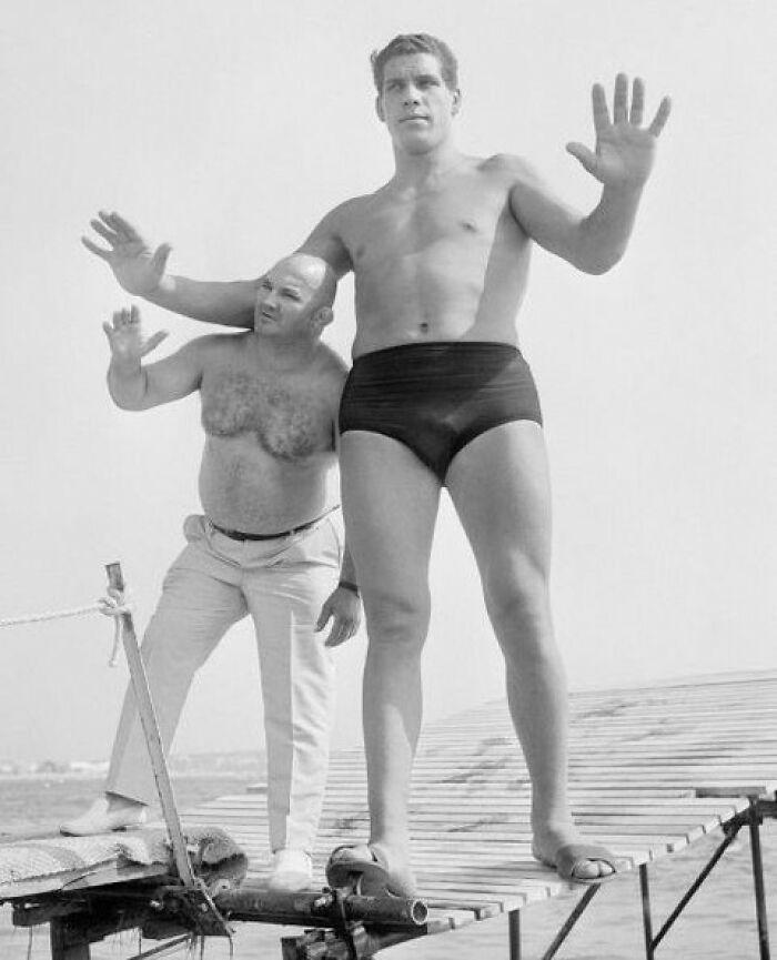 Historical photo showing the tallest man in history with a smaller man on a wooden dock