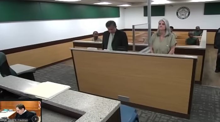 Cena de tribunal com casal em pé durante audiência em caso de disciplina pública