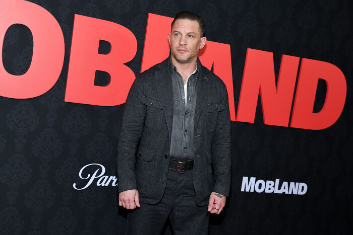 Tom Hardy posing in front of Mobland movie poster at premiere event Tom Hardy posing in front of Mobland movie poster at premiere event