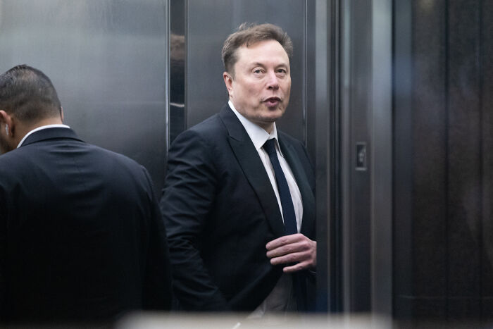 Elon Musk in a suit inside an elevator, reacting to 'The Odyssey' casting remark