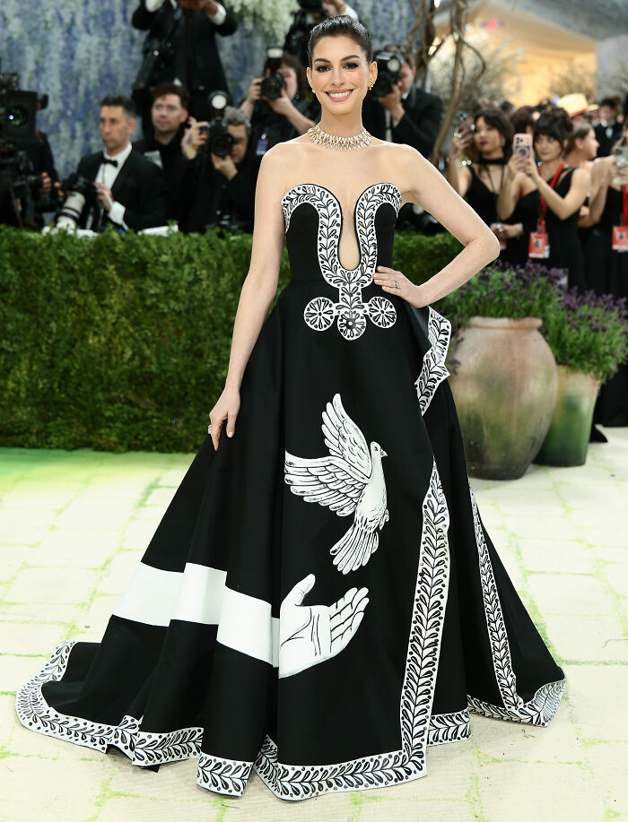 Anne Hathaway in one of the jaw-dropping outfits from the 2026 Met Gala, wearing a black strapless gown with white designs.