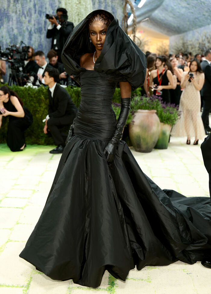 A striking model in a dramatic black gown with a voluminous hood and train at the 2026 MET Gala, showcasing incredible outfits.