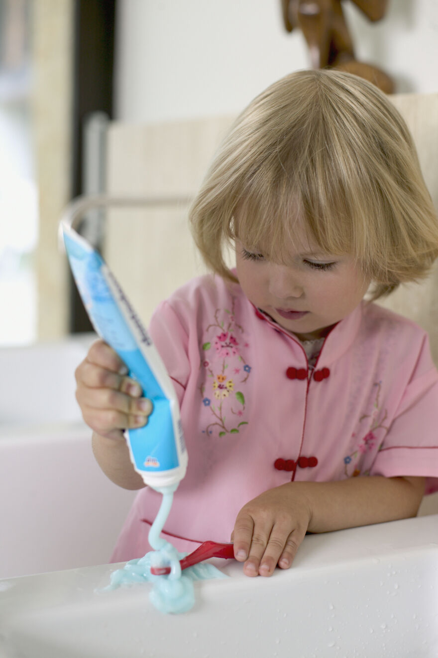 A young child in a pink top squeezing toothpaste onto a brush and sink, highlighting daily life changes from scientific breakthroughs.