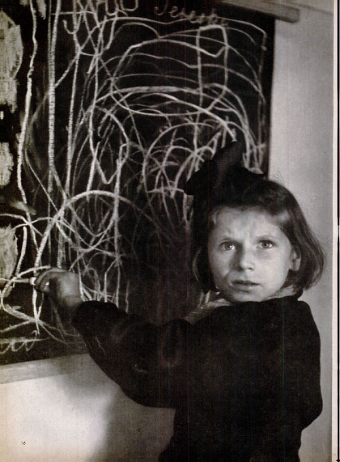 Black and white photo of young girl drawing chaotic chalk lines on blackboard
