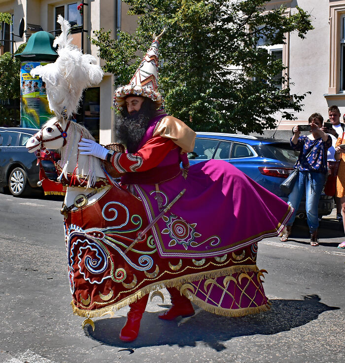 Man dressed in colorful traditional costume riding a fake decorated horse in street parade