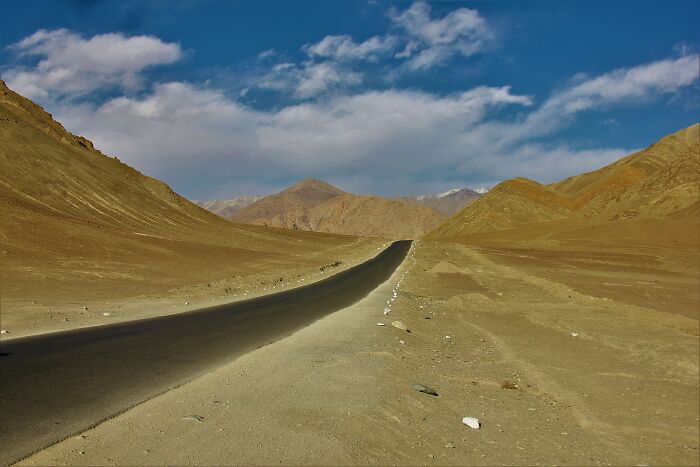 Empty road through arid hills under blue sky showing stunning desert views