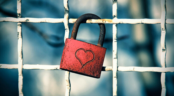 A rusty red padlock with a heart engraving on a white grid fence, evoking a sense of nostalgia.