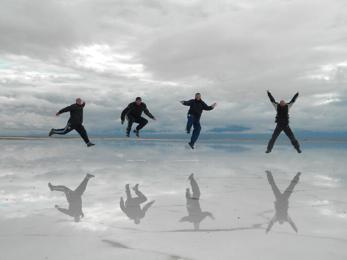 People jumping on reflective water surface creating mirrored silhouettes