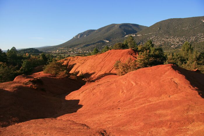 Red rocky terrain with green trees and distant mountains