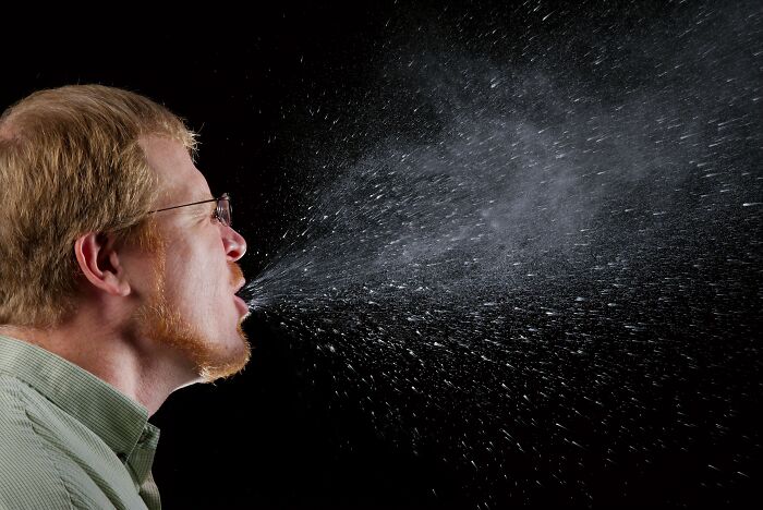 Man sneezing with visible droplets spreading in air