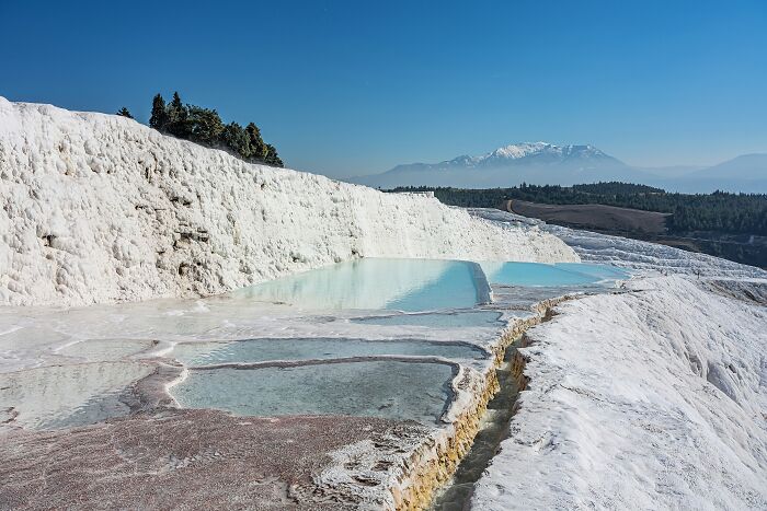 Terraced mineral pools in white travertine formations with mountain view